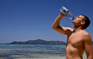 man drinking water on the beach from a bottle